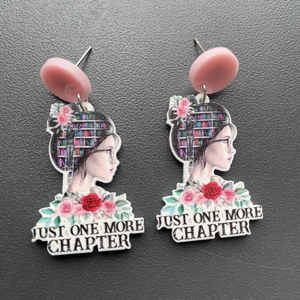 Close-up of acrylic book earrings featuring Just One More Chapter text and floral portrait