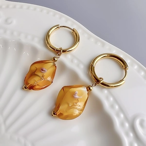 Close-up of vintage 18K gold hoop earrings with amber glass flower pendants on ceramic