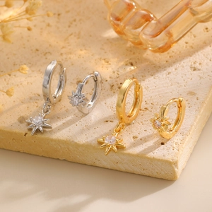 Exquisite gold and silver star earrings with zircons on a light stone textured surface