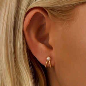 Detail of minimalist gold double-cross earrings with polished white pearl on a model