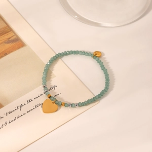 Detail of green stone beaded bracelet with golden heart pendant on aesthetic background