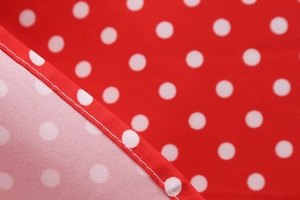 Close-up of high-quality white stitching and seam finish on red polka dot fabric dress