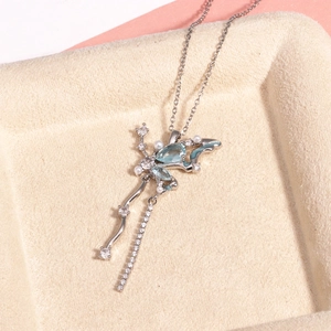 Détail macro du collier argenté avec gemme bleue, perle et zircon sur un plateau beige