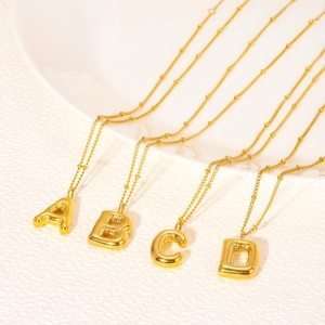 Golden bubble letter pendants A B C D on thin bead chains over a ceramic plate