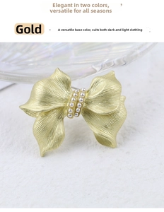 Detail of golden bow brooch featuring elegant double row pearls and brushed metal texture