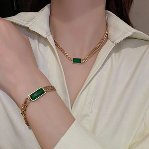 Détail d'un ensemble de bijoux en maille gourmette dorée avec une gemme vert émeraude
