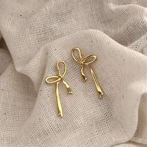 Macro shot of gold bow-shaped stud earrings on beige linen texture background