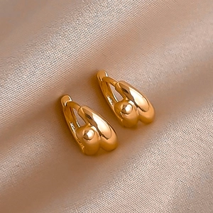 Close-up of chunky gold hoop earrings resting on smooth champagne silk fabric