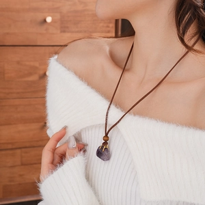 Close-up of a purple amethyst pendant on a brown leather cord worn with a white sweater