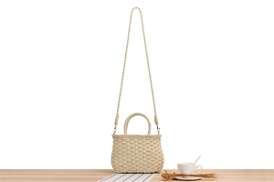 Detail of paper straw woven bag on wooden table with coffee cup for summer vacation vibe