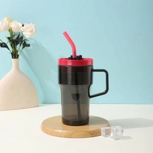 Gray translucent plastic straw cup with red lid and black handle on a wood base