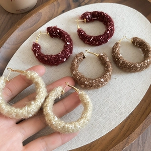Nahaufnahme von wollumwickelten Creolen in Burgunder, Braun und Creme auf einem Tablett