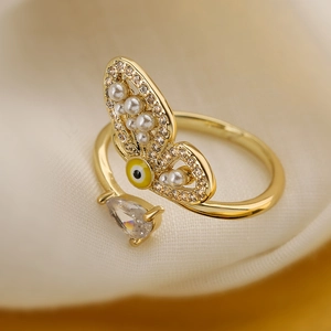 Macro shot of gold butterfly ring with pearl, zircon, and evil eye detail on satin