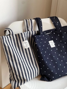 Détail de sacs cabas en toile denim avec rayures et pois posés sur une chaise blanche