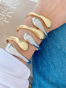 Polished gold and silver teardrop bracelets worn in a stylish stacked minimalist look