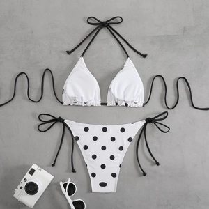 Flat lay of black and white polka dot bikini set with neck strap and side ties on stone surface