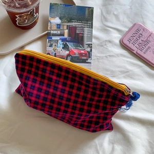 Detail of red and black checkered makeup bag with vibrant yellow zipper and blue tassel charm