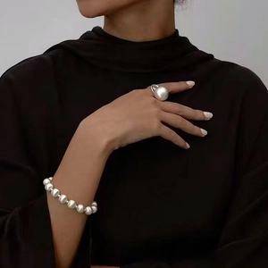 Détail du collier de perles et de la grande bague boule sur un col roulé noir