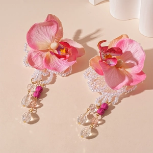 Detail of pink floral earrings with pearls and crystal bead tassels on a warm background