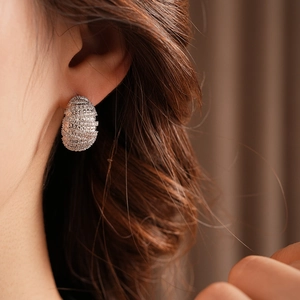 Close-up of a silver-colored oval earring with pave-set cubic zirconia on a model ear