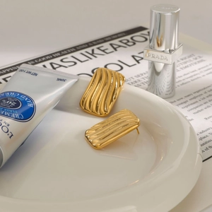 Gros plan de boucles d'oreilles rectangulaires dorées avec texture ondulée sur porcelaine