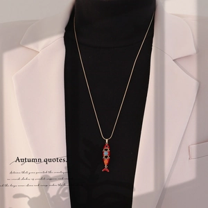 Detailed close-up of a vintage red koi fish pendant on a gold chain worn over a blazer