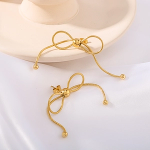 Golden bow earrings with snake chain tassels and bead ends on minimalist silk background