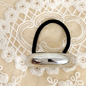 Close-up of polished silver metal buckle and black elastic hair tie on white lace fabric