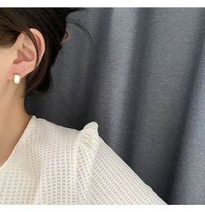 Close-up of geometric gold huggie earrings with white mother of pearl inlay on model ear