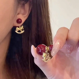 Retro style wine red pearl stud earrings with a gold rocking horse pendant on a model