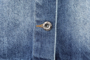 Close-up of vintage silver button with Jeans text and blue washed denim fabric texture