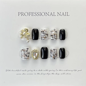 Detalle de uñas postizas hechas a mano en blanco y negro con lazos dorados y perlas