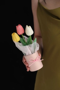 Close-up of a hand holding three colorful PU tulips in a pink pot with a bow