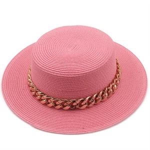 Detailed texture of pink straw boater hat with stylish chunky gold chain decoration