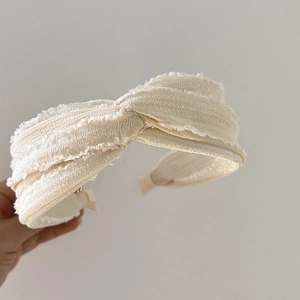 Detail of a beige French-style knotted headband with fringe texture and soft fabric finish