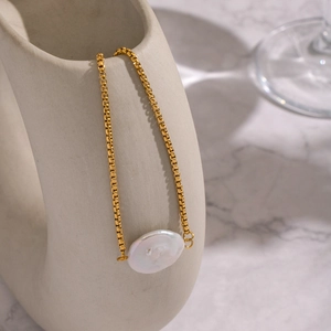 Detailed macro view of a baroque pearl pendant on a gold box chain over ceramic art