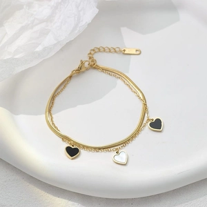Pulsera dorada de doble capa con cadena de serpiente y colgantes de corazón en plato blanco