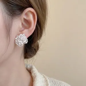 Elegant white 3D floral pearl stud earrings with textured petals worn by a model