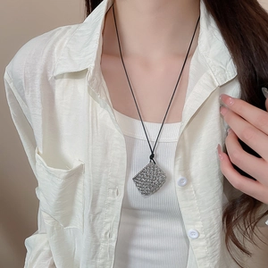 Macro shot of a silver woven hollow cube pendant on a black minimalist cord necklace