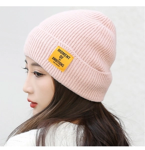 Detail shot of a pink knitted beanie featuring a yellow embroidered quote label