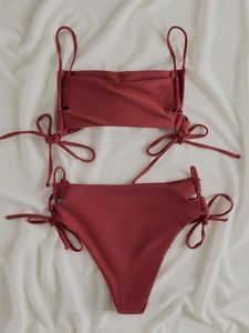 Close-up of rust red bikini set with side tie details on textured cream fabric