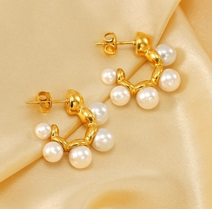Macro detail of gold plated C-shape earrings with six pearls on champagne silk fabric