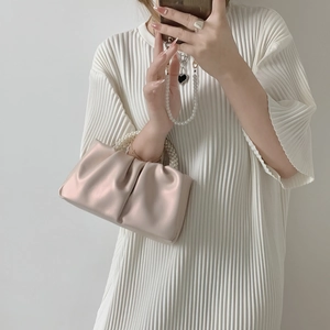 Beige pleated cloud handbag with pearl bead handle held by a model in a white dress
