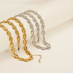 Détail de colliers en coquillage or et argent enroulés sur un support blanc cylindre