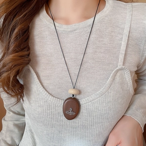 Close-up of geometric acrylic and wood pendant necklace on a ribbed knit sweater
