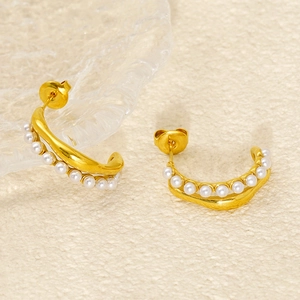 Detail shot of golden C-shaped stainless steel earrings with white pearls on warm background