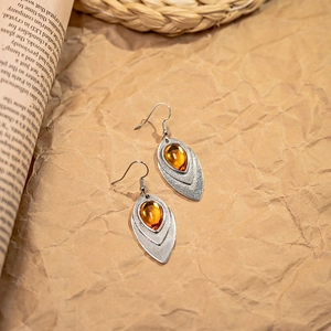 Close-up of bohemian leaf earrings with silver metal and amber teardrop resin stones