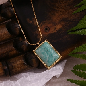 Detail of a rectangle green natural stone pendant with a gold plated chain on a wood hand