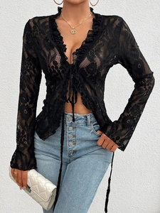 Detail of black floral lace fabric with ruffled edges and tie-up front on long sleeve top