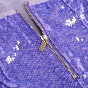 Dettaglio del tessuto con paillettes viola e cerniera in metallo dorato sull'abito